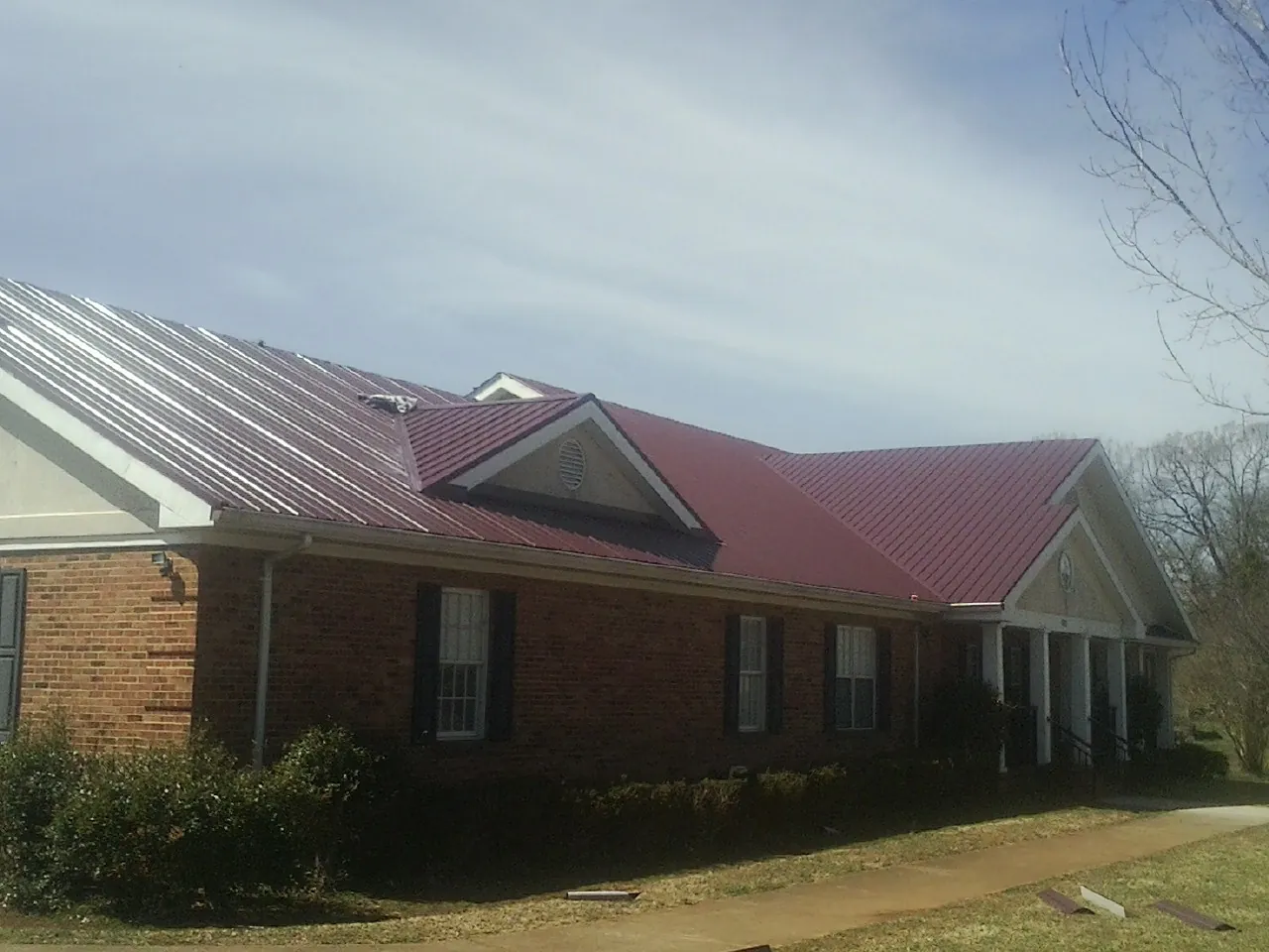 Red metal roof with gabled entries on a long brick building, from a Hail Damage Roof Repair job in Beverly